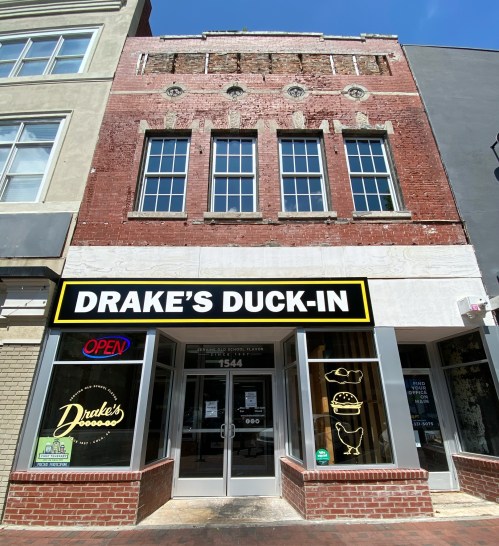 Exterior of Drake's Duck-In, a restaurant with a bright sign, large windows, and a brick facade on a sunny day.