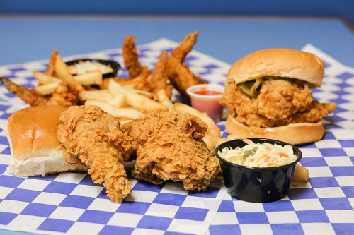 A plate of fried chicken, a sandwich, fries, and coleslaw on a blue checkered tablecloth.