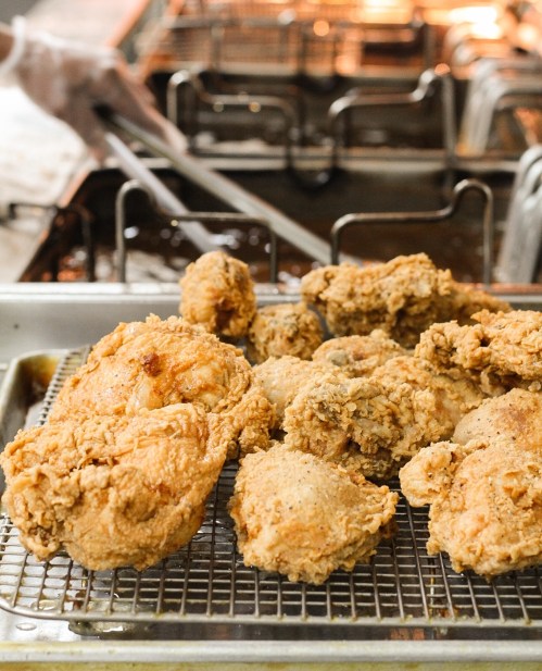 Crispy fried chicken pieces on a cooling rack, with a fryer in the background.
