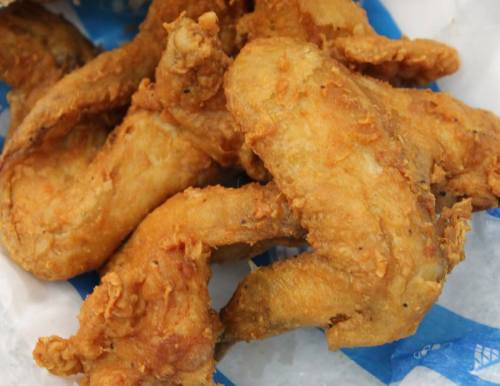 A close-up of crispy, golden-brown fried chicken wings on a blue paper background.