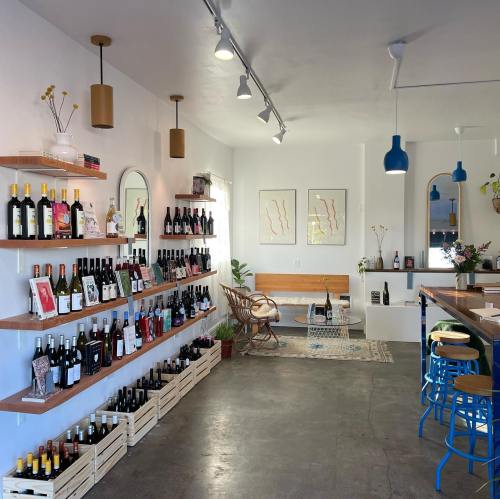 A modern wine shop interior with shelves of wine bottles, a seating area, and artistic wall decor.