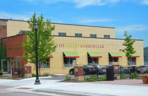 A bookstore named "The Valley Bookseller" with green awnings, surrounded by trees and parked cars.