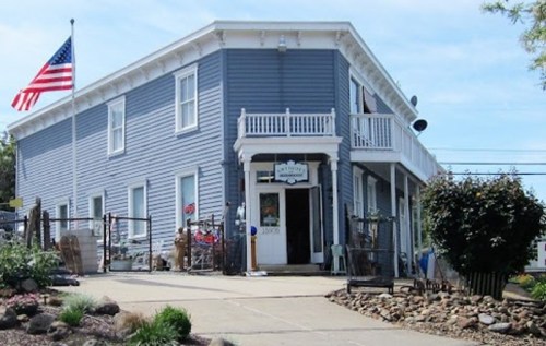 A blue two-story building with an American flag, featuring a front porch and garden area.
