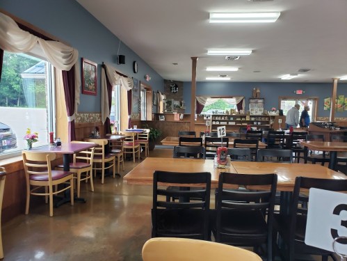 Cozy restaurant interior with wooden tables, chairs, and large windows, featuring a casual dining atmosphere.