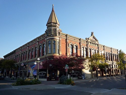 Historic building with ornate architecture, featuring a pointed tower and colorful storefronts, surrounded by trees.