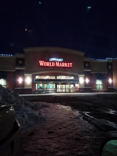 Exterior of a World Market store at night, illuminated sign, snow on the ground, and parking lot visible.