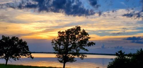 A serene sunset over a calm lake, with silhouetted trees against a colorful sky.
