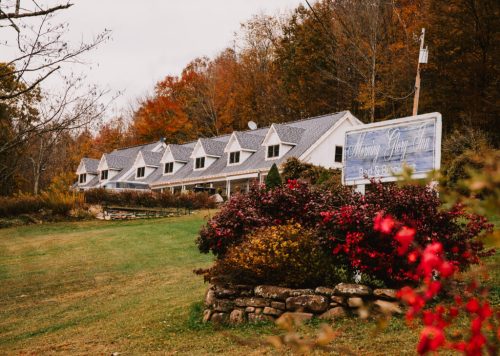 A charming bed and breakfast with a sign, surrounded by colorful autumn foliage and blooming flowers.