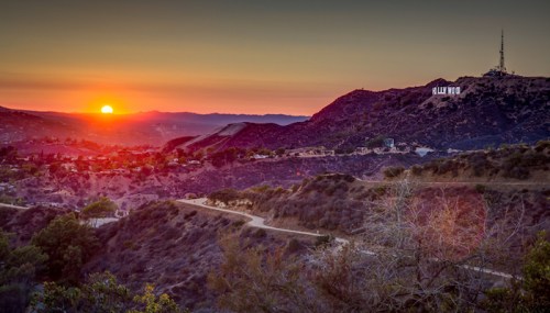 Sunset over hills with the Hollywood sign in the distance, casting a warm glow on the landscape.
