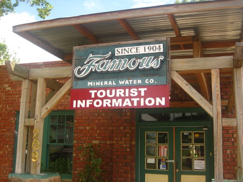 Sign for "Famous Mineral Water Co." with "Tourist Information" below, featuring a rustic wooden structure.
