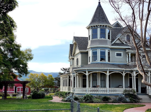 A large, elegant Victorian-style house with a turret, surrounded by greenery and a scenic landscape.