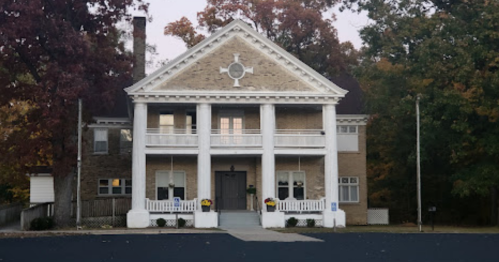 A large, historic building with a grand entrance, white columns, and autumn foliage in the background.