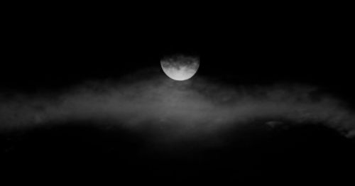 A full moon partially obscured by dark clouds in a black and white night sky.