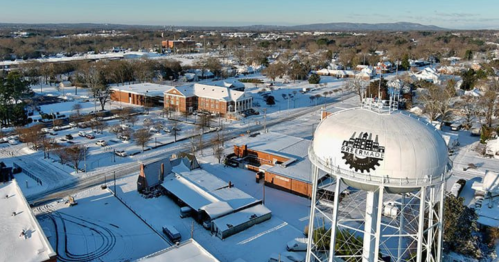 A snowy landscape featuring a water tower, buildings, and trees, with a clear sky in the background.