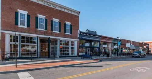 Historic brick buildings line a street, featuring shops and outdoor seating under a clear blue sky.