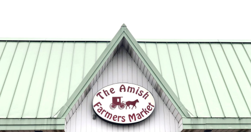 Sign for "The Amish Farmers Market" on a building with a green roof and white siding.