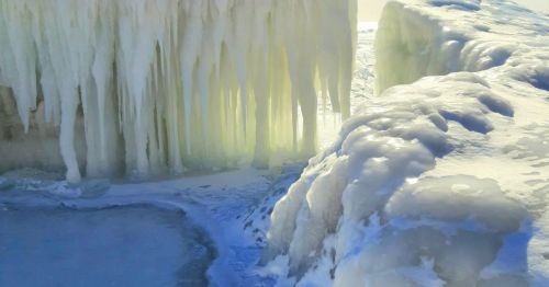 Icicles hang from a frozen surface, with a shimmering icy landscape in the background.