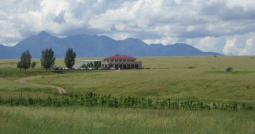 A large building sits in a grassy field with mountains in the background under a cloudy sky.