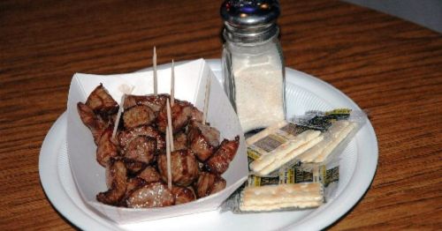 A plate of grilled meat skewers with salt, crackers, and condiments on a wooden table.
