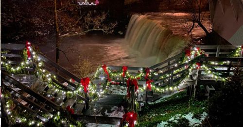 A beautifully lit waterfall at night, adorned with festive lights and red bows along the wooden railing.