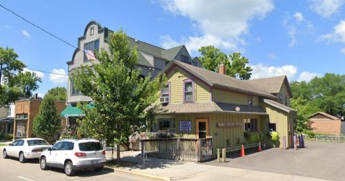 A charming two-story building with a green exterior, surrounded by trees and parked cars, under a blue sky.