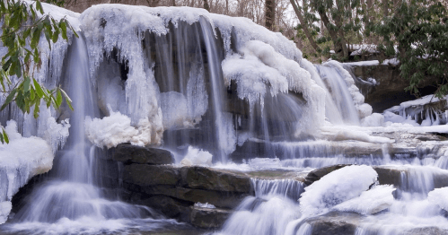 A frozen waterfall surrounded by ice and snow, with flowing water visible beneath the icy surface.