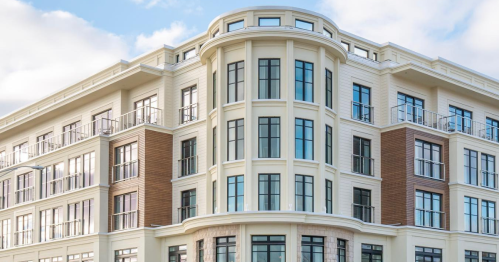 Modern multi-story building with large windows and a curved facade, set against a blue sky.