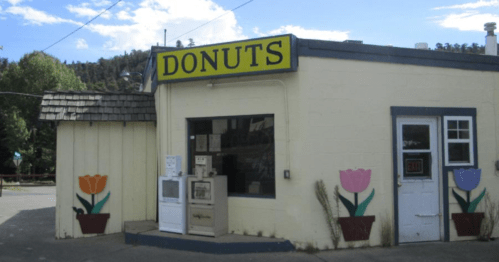 A small donut shop with a bright yellow sign, featuring flower murals on the walls and a rustic exterior.