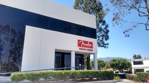 Exterior of the Fender Visitor Center, featuring a large sign and modern architecture against a clear blue sky.
