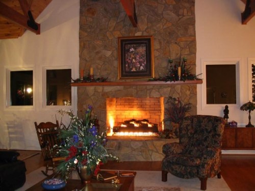 Cozy living room with a stone fireplace, floral arrangement, and comfortable seating under wooden beams. Warm ambiance.
