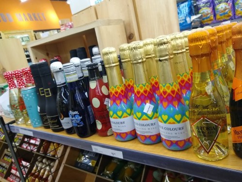 A shelf displaying various bottles of sparkling wine and beverages, featuring colorful labels and packaging.