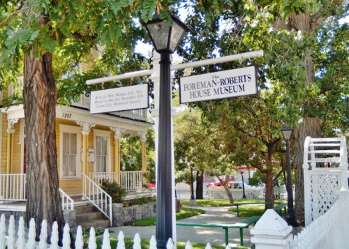 Sign for the Foreman-Roberts House Museum, with a historic yellow house and trees in the background.
