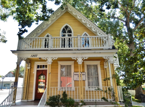 A charming yellow Victorian house with white trim, featuring a gabled roof and decorative balcony.