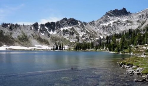 A serene mountain lake surrounded by rocky peaks and lush greenery under a clear blue sky.