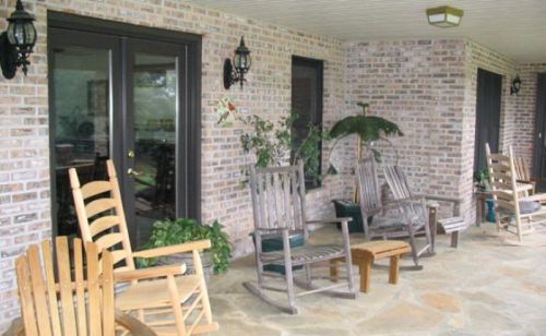 A cozy porch with wooden rocking chairs, potted plants, and brick walls, creating a welcoming outdoor space.