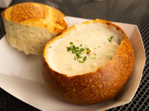 A bread bowl filled with creamy soup, garnished with herbs, alongside a piece of crusty bread.