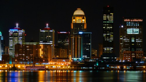 Nighttime city skyline with illuminated buildings reflecting on water.