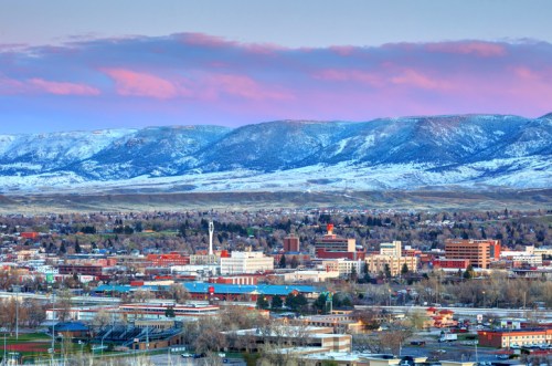 A panoramic view of a city with mountains in the background, featuring buildings and a colorful sky at sunset.