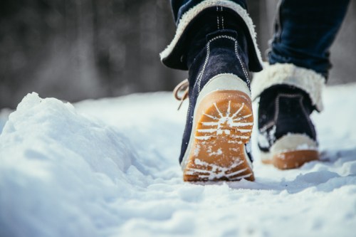 A person walking in snow, wearing dark boots with a fur lining, leaving footprints in the fresh snow.