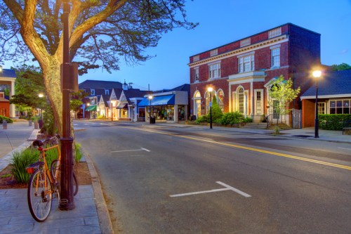 A quiet street at dusk, featuring a brick building, shops, and a parked bicycle near a tree.