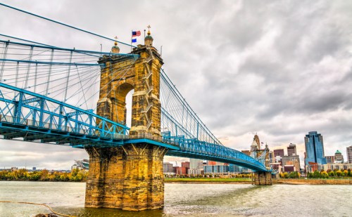 Cincinnati's John A. Roebling Suspension Bridge spans the Ohio River, with a cloudy skyline in the background.
