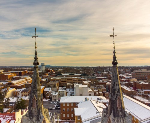 Snow-covered rooftops and church spires against a cloudy sky, with a distant view of a cityscape.