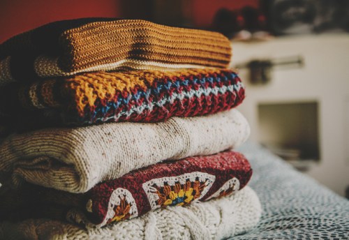 A neatly stacked pile of colorful knitted sweaters on a textured surface, with a cozy background.