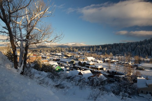 A snowy landscape view of a small town surrounded by trees and mountains under a clear blue sky.