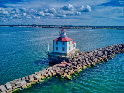 A lighthouse on a rocky pier, surrounded by calm blue waters and a partly cloudy sky.