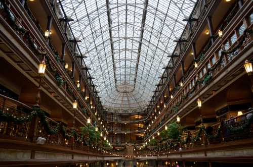 A grand indoor space with a glass ceiling, decorated with greenery and lights, showcasing elegant architecture.