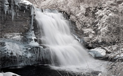 A serene waterfall surrounded by icy rocks and frosted trees, creating a tranquil winter scene.