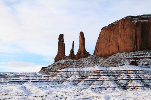 Snow-covered landscape with towering red rock formations under a blue sky.