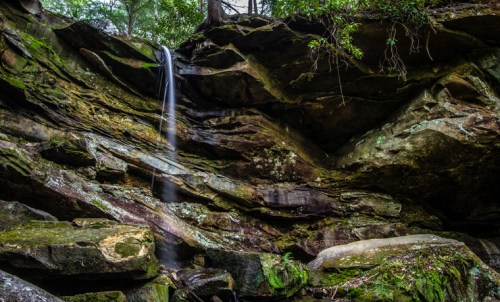 A serene waterfall cascading down rocky cliffs, surrounded by lush greenery in a tranquil forest setting.