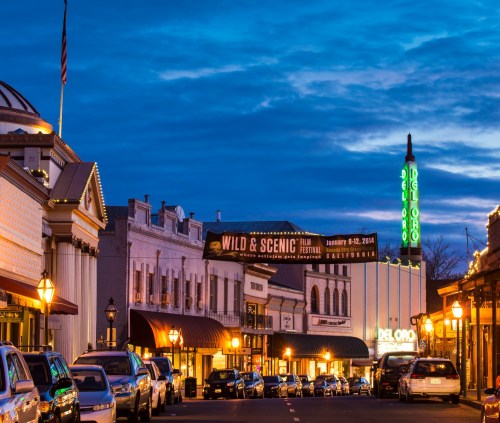 A charming street scene at dusk featuring historic buildings, vintage cars, and a neon theater sign.